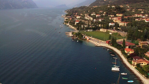 A coastal town with buildings along the shoreline, boats docked, and mountains in the background. - Rustico at south shore of Lake Garda (Costermano)