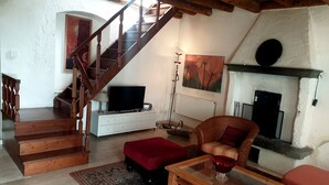 A living room with a wooden staircase, a television on a white cabinet, a red armchair, a glass coffee table, and a fireplace. - Rustico at south shore of Lake Garda (Costermano)