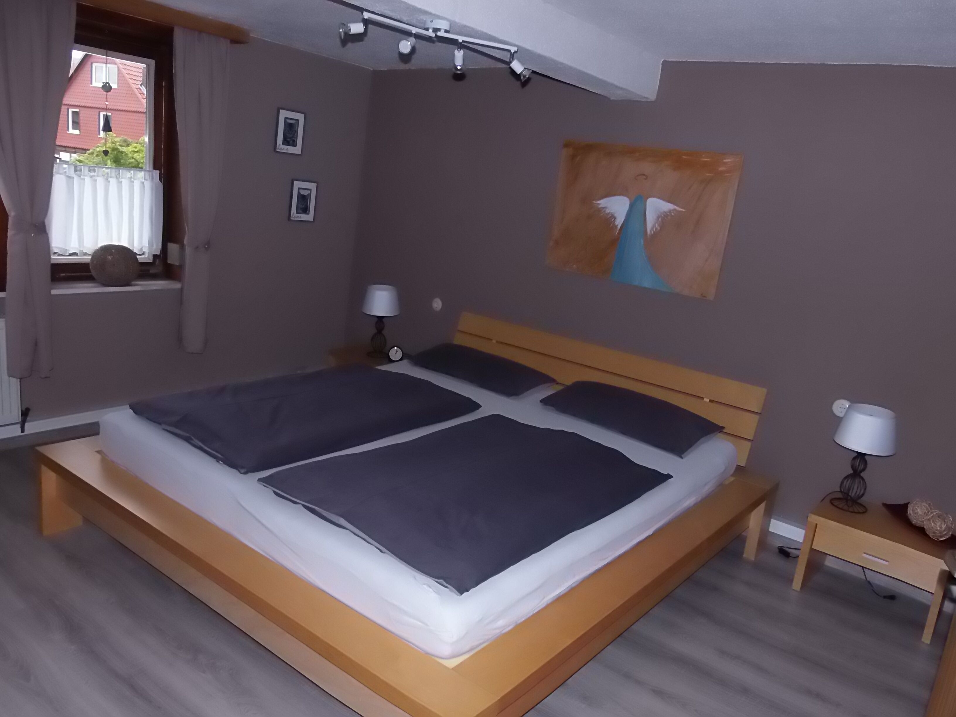 Een slaapkamer met een houten bed, twee nachtkastjes, een wandlamp en een schilderij.