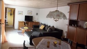Una sala de estar con un sofá negro, una mesita con velas, un televisor y un mueble de madera.