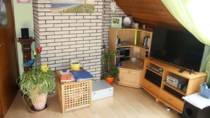 A cozy living room with a brick fireplace, wooden entertainment center, and a large flat-screen TV. - Cozy holiday apartment in Kirchlengern in a quiet residential area (Kirchlengern)