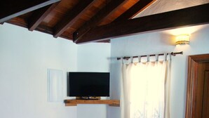 Un dormitorio con cama, una mesita, televisor montado en la pared y una puerta.