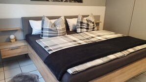 Een moderne slaapkamer met een houten bedframe, een zwart-wit geruit beddegoed en een grijs hoofdbord.