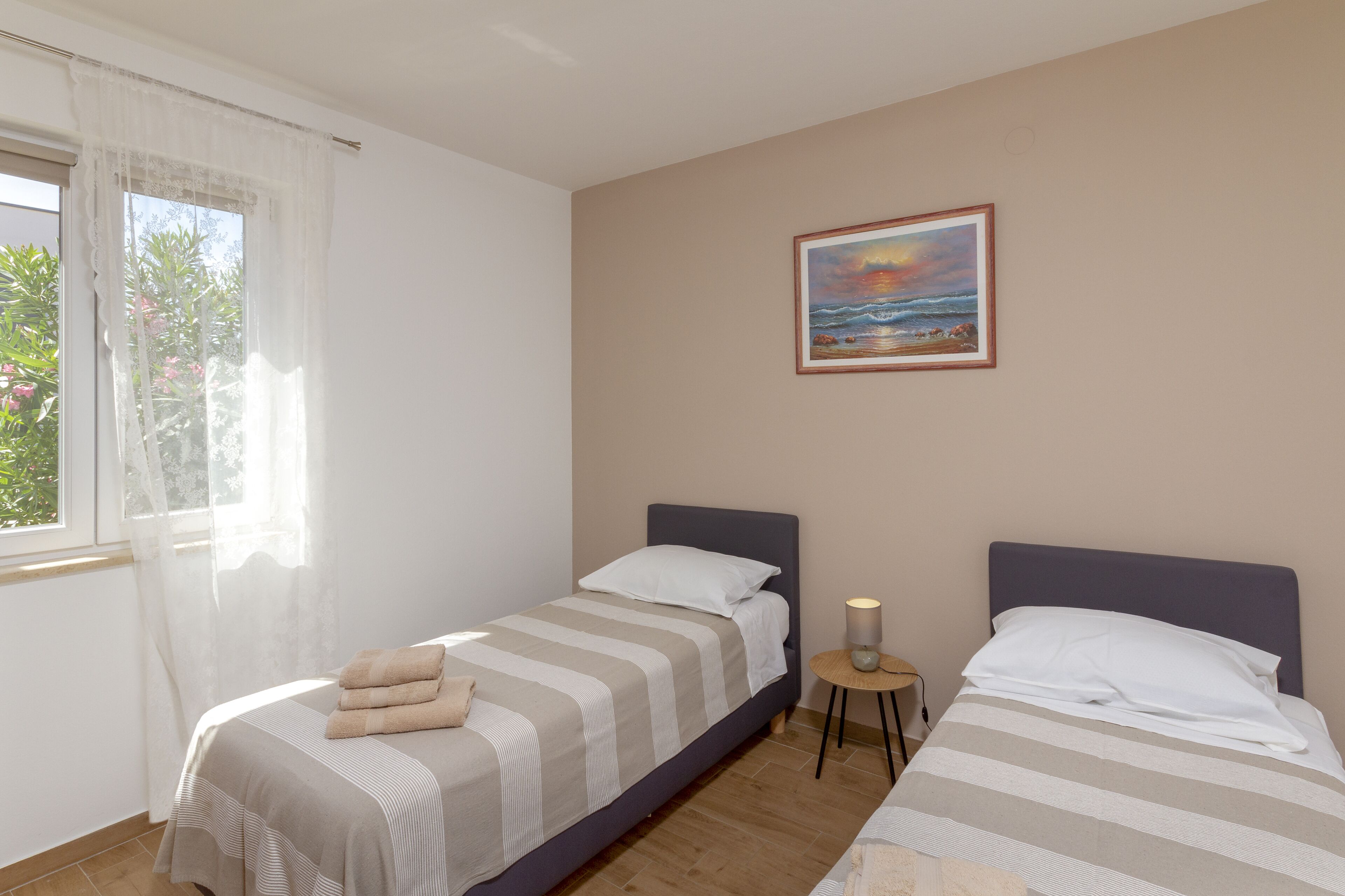 Un dormitorio con dos camas, un cuadro en la pared y una ventana con cortinas traslúcidas.