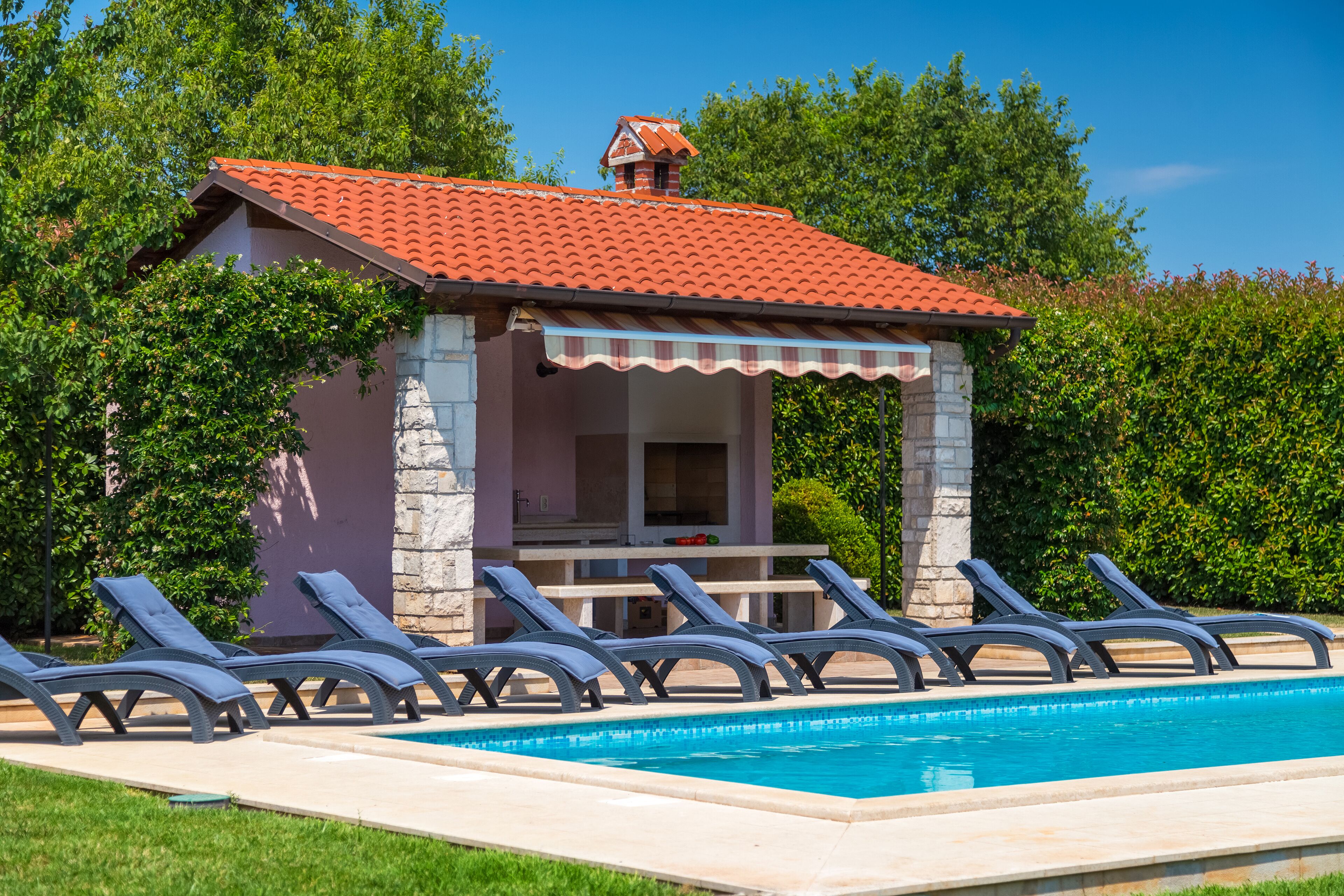 A poolside area with lounge chairs and a small building with a red-tiled roof.