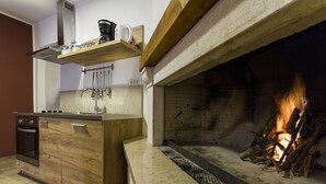 Een moderne keuken met een inbouwoven, houten kastjes, een marmeren aanrechtblad en een open haard met vuur.