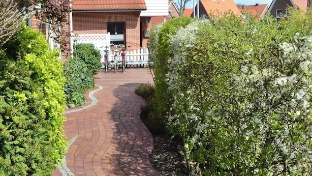 A residential area with a brick house, a paved pathway, and a flag. - Daub's island oasis/apartment with terrace also possible with dog (Borkum)