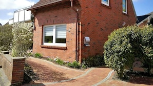 A red brick house with a tiled roof, a front window with shutters, and a small garden with a pathway leading to the entrance. - Daub's island oasis/apartment with terrace also possible with dog (Borkum)