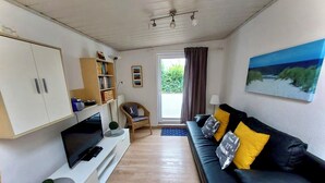 A living room with a black sofa, a TV, a bookshelf, and a painting on the wall. - Daub's island oasis/apartment with terrace also possible with dog (Borkum)