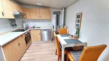 Eine kleine Küche mit Holzausstattung, einem Geschirrspüler und einem Essbereich mit Korbstühlen und einem Tisch.