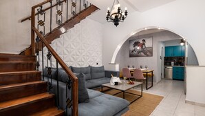 Una sala moderna con un sofá gris, una escalera de madera y una zona de cocina con armarios azul verdosos.