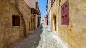 Una estrecha calle adoquinada bordeada por edificios históricos con muros de piedra y contraventanas de madera.