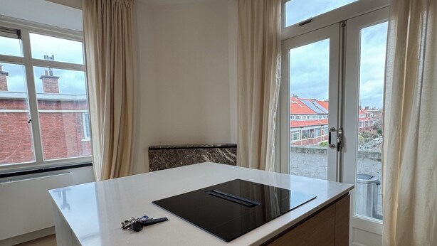 Una cocina moderna con una isla central, armarios de madera y ventanas amplias con cortinas.