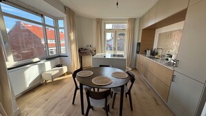 Una cocina moderna con armarios de madera, una mesa de comedor con individuales y ventanas grandes con cortinas.
