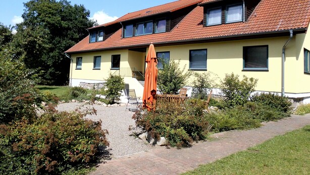 Una casa a due piani con tetto in tegole rosse, facciata gialla e vialetto sterrato.