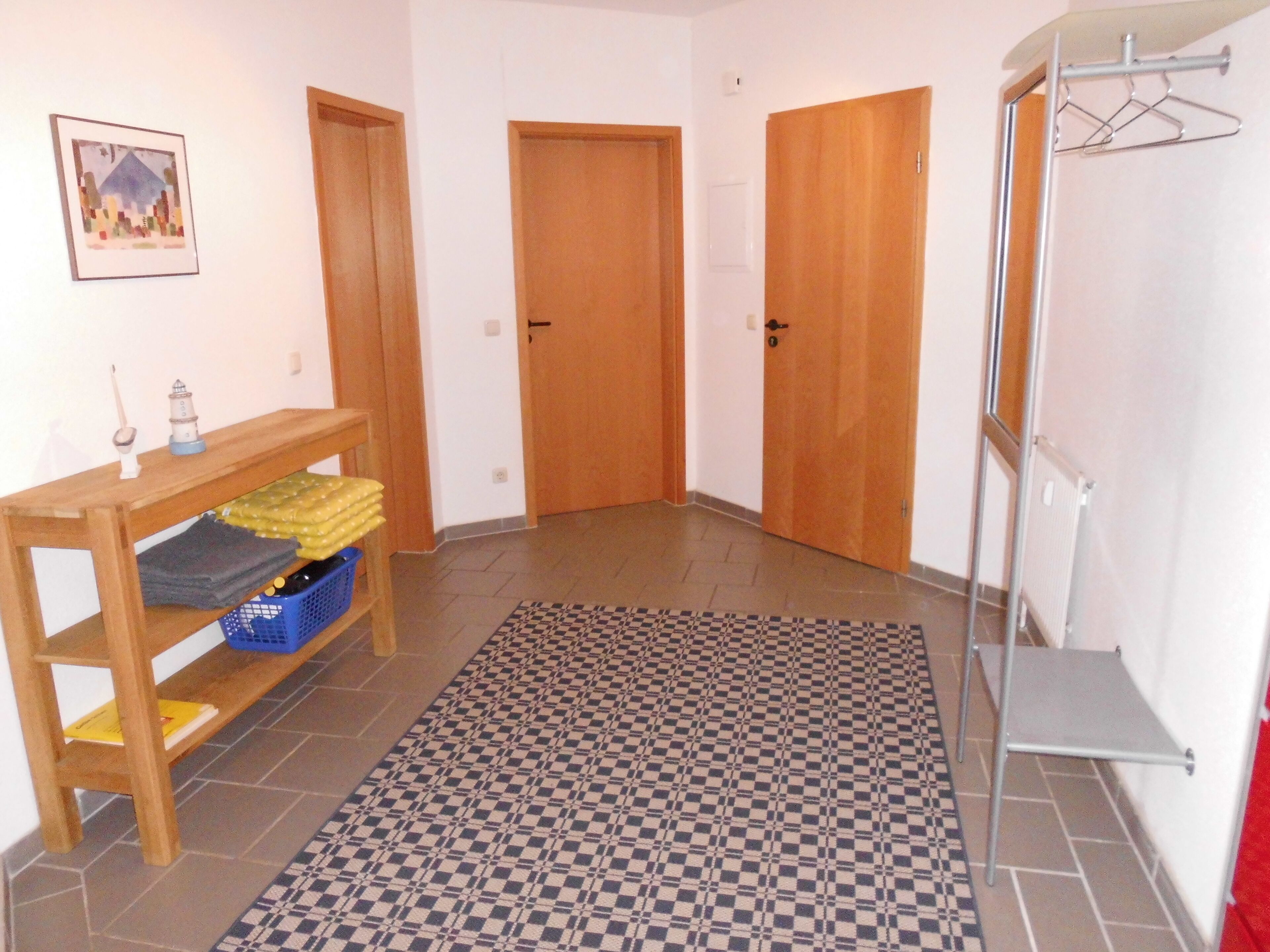Ein Flur mit Holztüren, einem Schachbrettteppich, einem Holztisch mit Körben und einem an der Wand befestigten Wäscheständer.