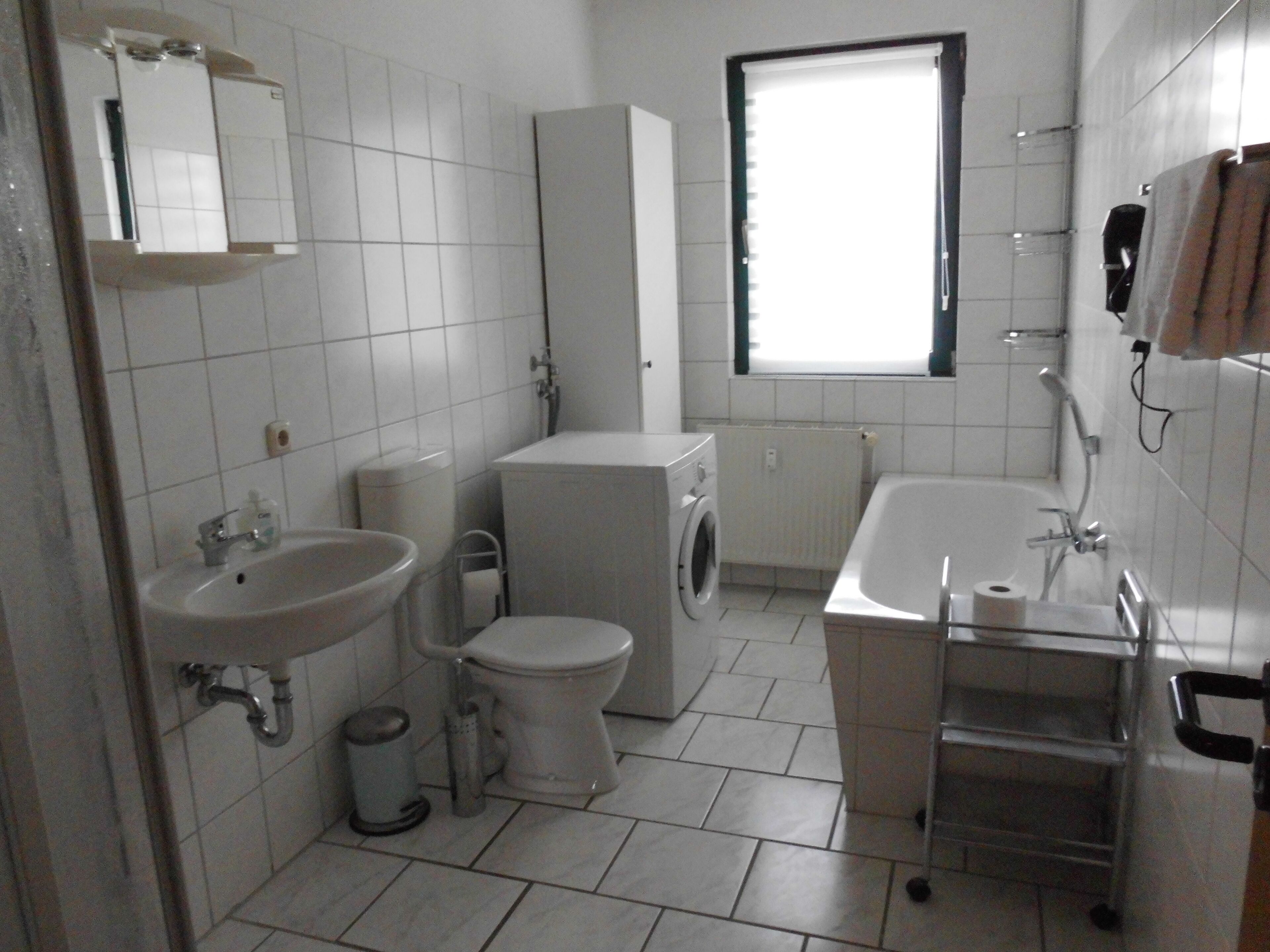 Ein kleines, sauberes Badezimmer mit Waschbecken, Toilette, Waschmaschine und Badewanne.