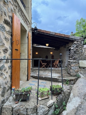 A rustic stone building with a wooden door, outdoor seating, and potted plants.