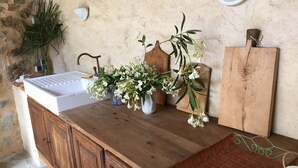 A wooden counter with a white sink, two vases with white flowers, a wooden cutting board, and a wall-mounted light fixture.