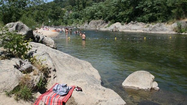 A natural setting with a river, rocks, and a blanket on a rock.