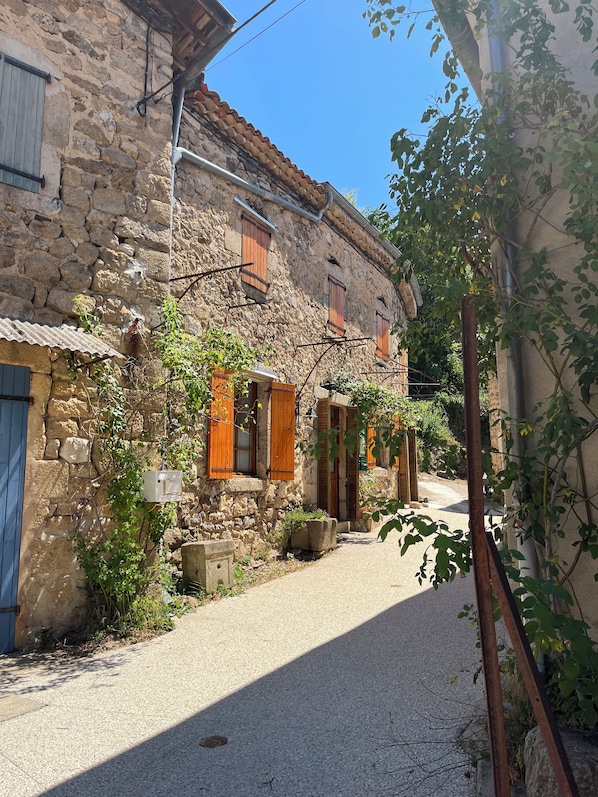 A narrow street with stone buildings, wooden shutters, and a clear sky.