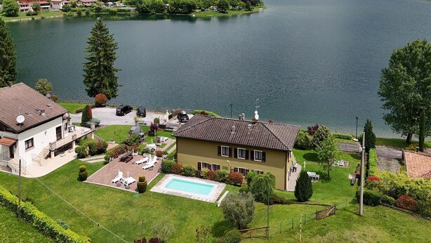 Una propiedad frente al lago con piscina, cancha de tenis y vistas al lago y las montañas.