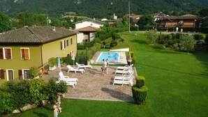 Una propiedad residencial con piscina, un patio con sillas de descanso y vistas a montañas verdes al fondo.