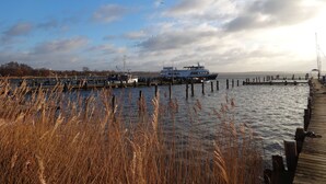 Eine Anlegestelle mit einem Boot, ein Steg, der sich ins Wasser erstreckt, und ein bewölkter Himmel.