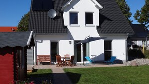 Ein zweistöckiges Haus mit geneigtem Dach, Solaranlagen und einer überdachten Terrasse mit Gartenmöbeln.