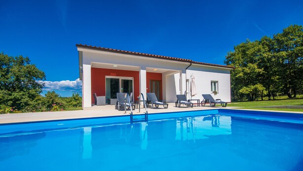 Une villa moderne dotée d’une piscine, d’un espace extérieur aménagé et d’un toit recouvert de tuiles rouges.