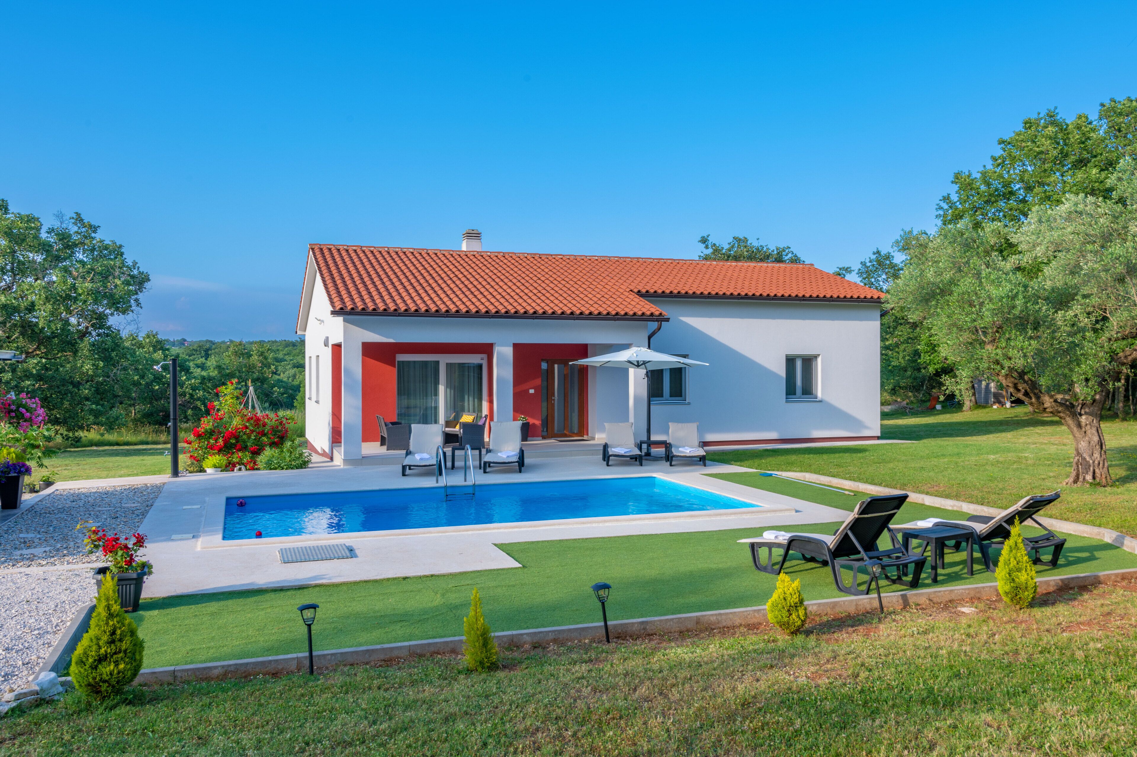 Una casa moderna con piscina, mobiliario de exterior y un jardín bien cuidado.