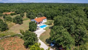 Une maison avec une piscine, entourée d’une forêt dense.
