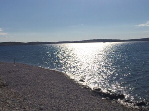 A pebbled beach with a calm sea and a distant shoreline.