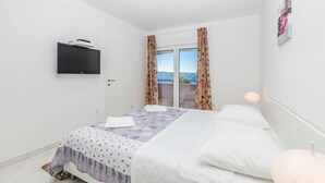 Une chambre à coucher avec un lit, un téléviseur fixé au mur, une porte et une fenêtre avec des rideaux.