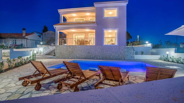 Une maison moderne à deux étages, dotée d’une piscine et de chaises longues.
