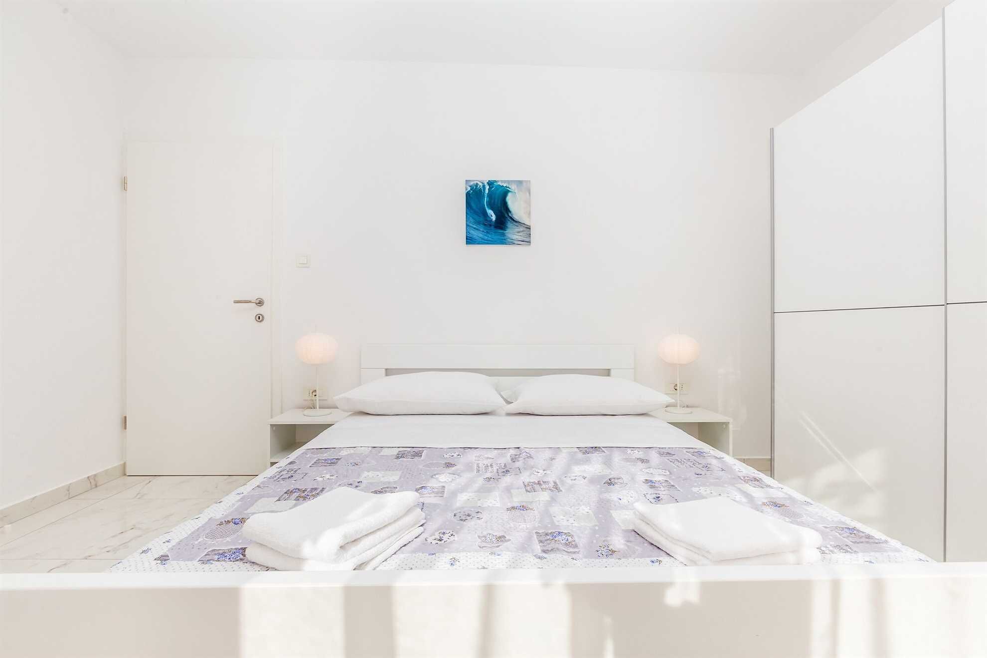 A minimalist bedroom with a bed, two bedside lamps, a painting on the wall, and a wardrobe.