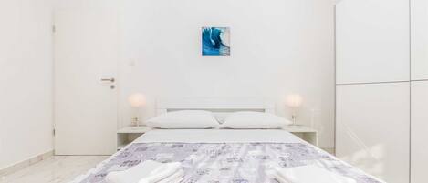 A minimalist bedroom with a bed, two bedside lamps, a painting on the wall, and a wardrobe.