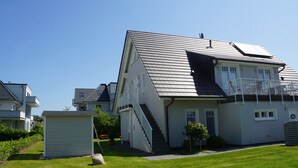 Moderni, kaksikerroksinen talo, jossa on kalteva katto, näkyvät portaat, jotka johtavat yläkertaan, sekä pieni etupiha, jossa on kivi ja puu.