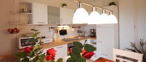 A modern kitchen with white cabinets, a wooden countertop, and a hanging light fixture.