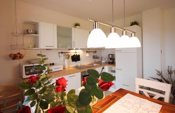 A modern kitchen with white cabinets, a wooden countertop, and a hanging light fixture. - Ren. Apartment on the ground floor, WiFi, close to the beach, partially fenced, children-u. tierfreundl. (Börgerende-Rethwisch)