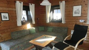 Interior acogedor de una cabaña con un sofá estampado, una mesa de centro de madera, una mecedora y una ventana con cortinas.