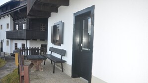 Un edificio con puerta y ventanas negras, una banca y una mesa en el exterior.