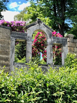 A stone archway with blooming pink flowers in a lush garden setting.