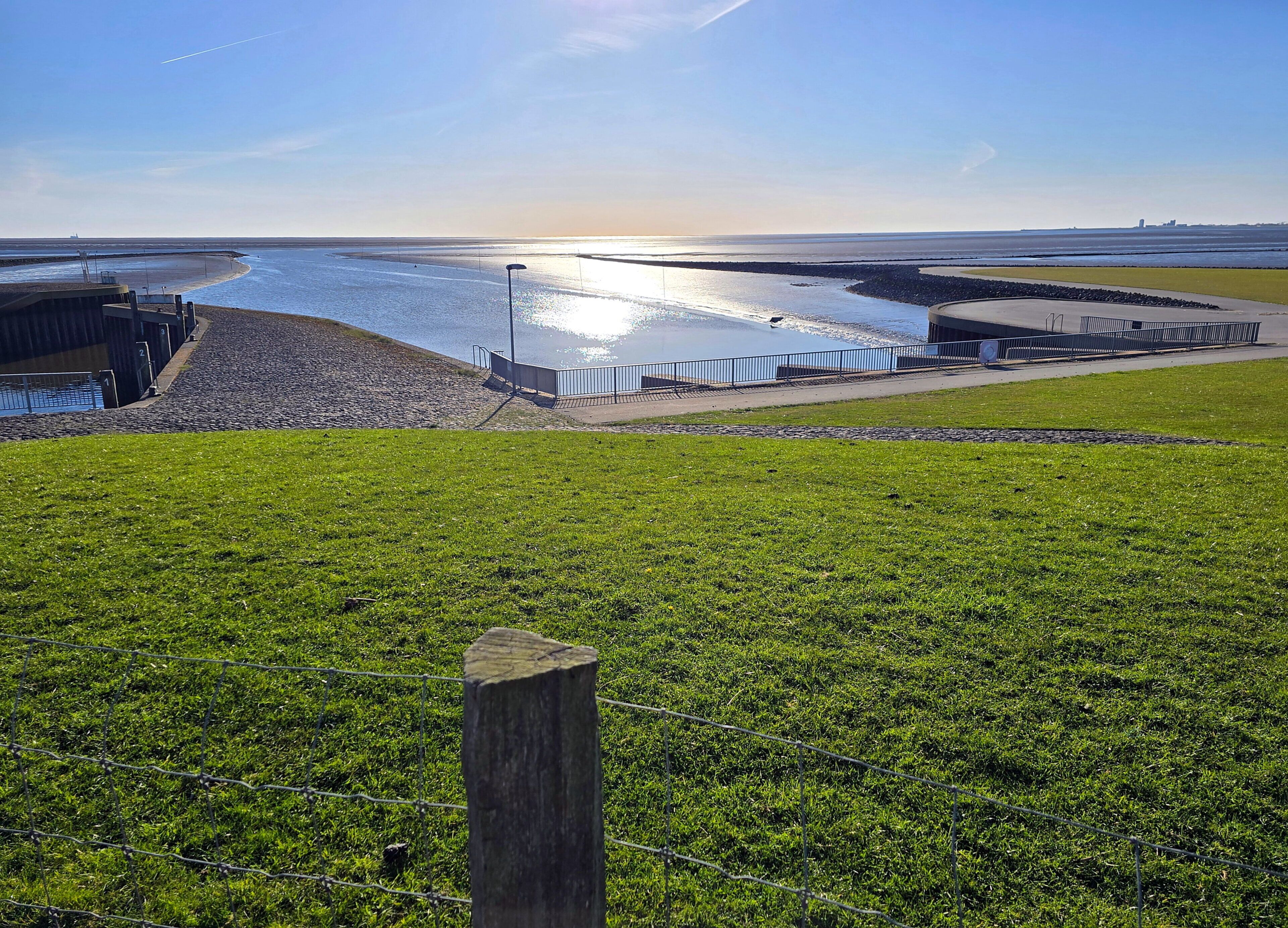 A coastal landscape with a grassy foreground, a sandy beach, and a body of water reflecting sunlight.