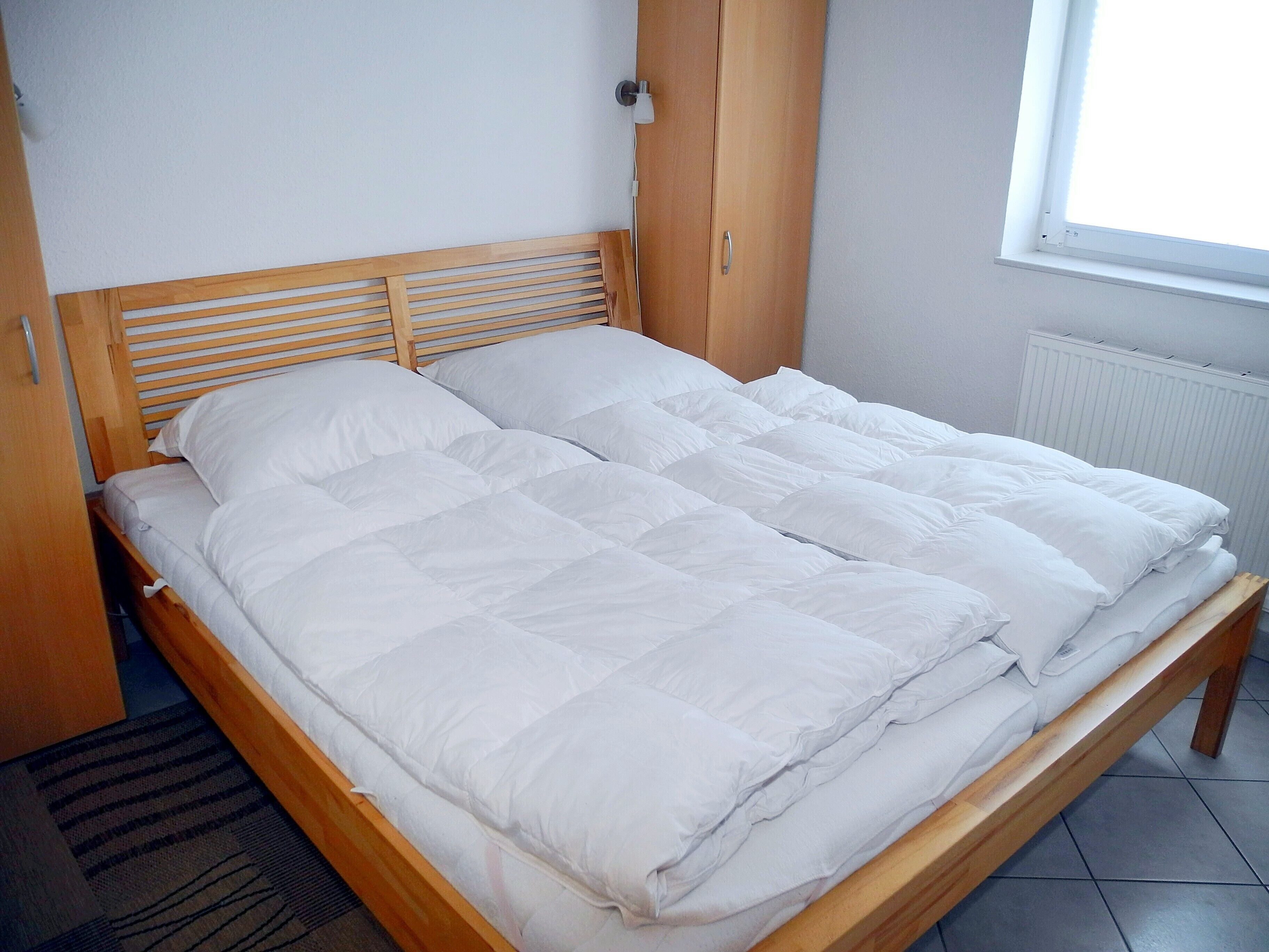 A single-bed room with a wooden headboard, a window with blinds, and a radiator.
