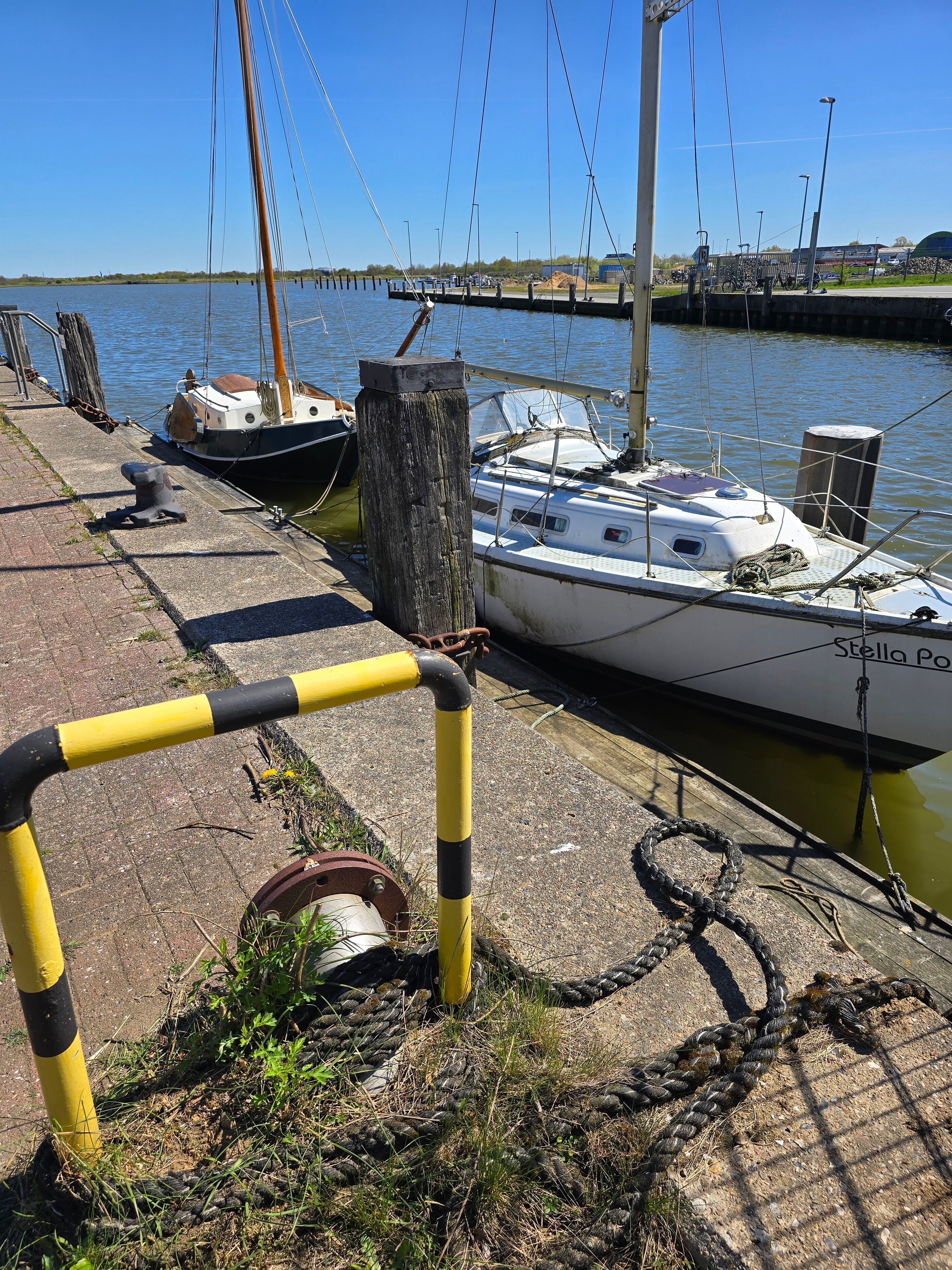 Un puerto deportivo con barcos amarrados, un poste de madera y un bozal amarillo.
