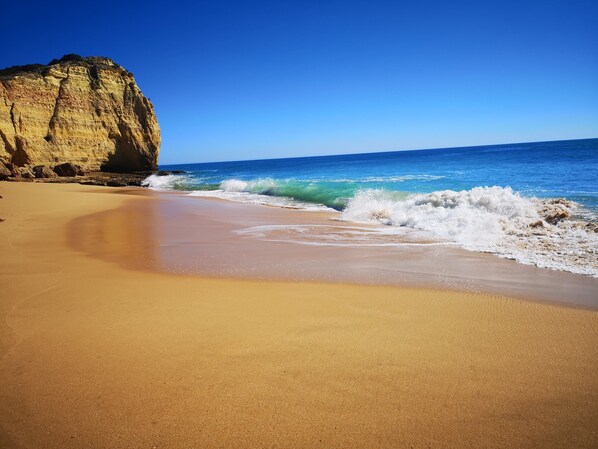 Une plage avec une grande formation rocheuse et des vagues qui déferlent sur le rivage.