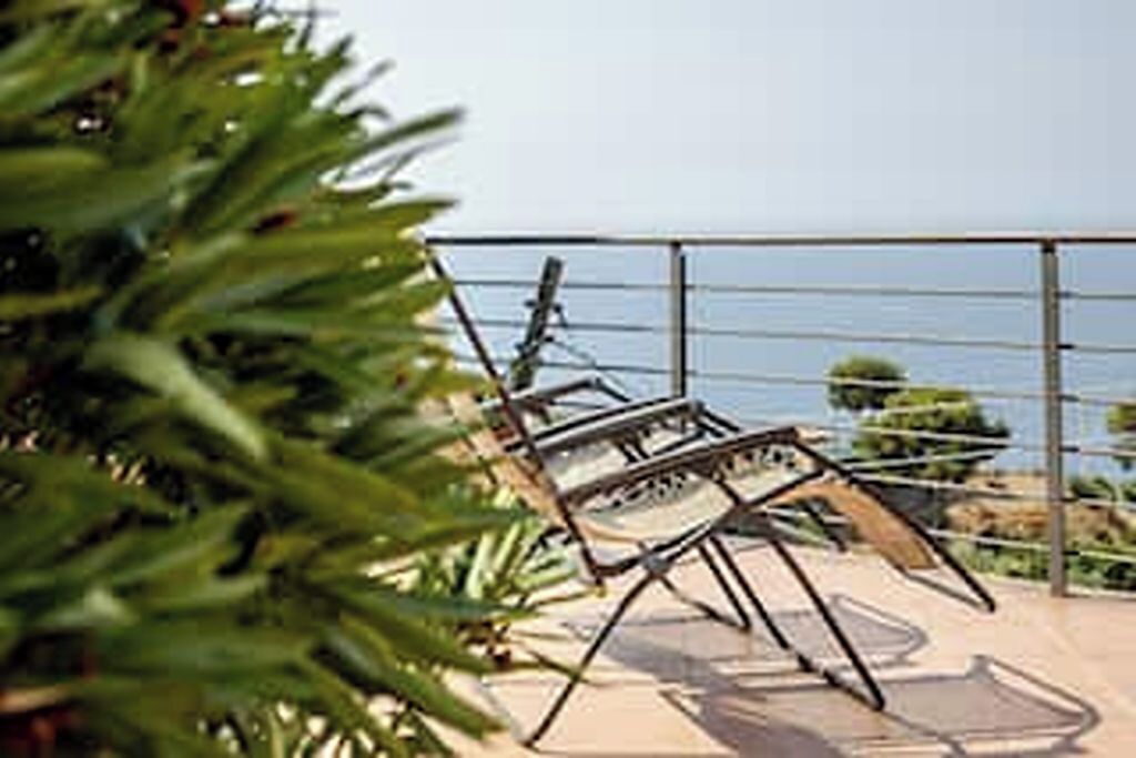 A balcony with outdoor seating and a view of the sea.