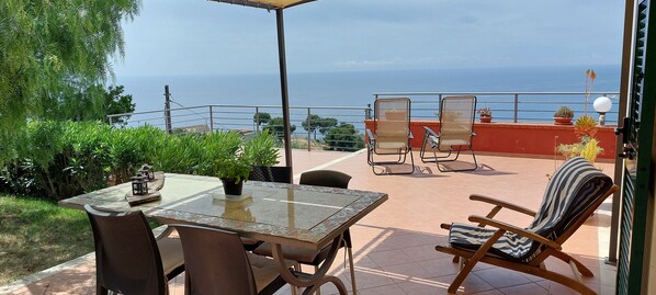 Une terrasse avec une table et des chaises, une vue sur la mer et des plantes en pot.