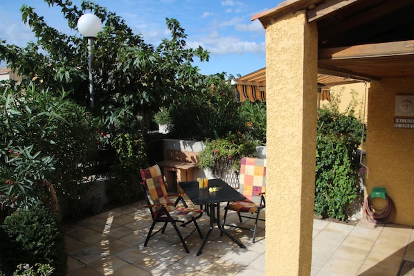 An outdoor patio area with a table and chairs, surrounded by lush greenery and a pergola structure. - Bright, cosy and lovingly arranged new residence (Narbonne)